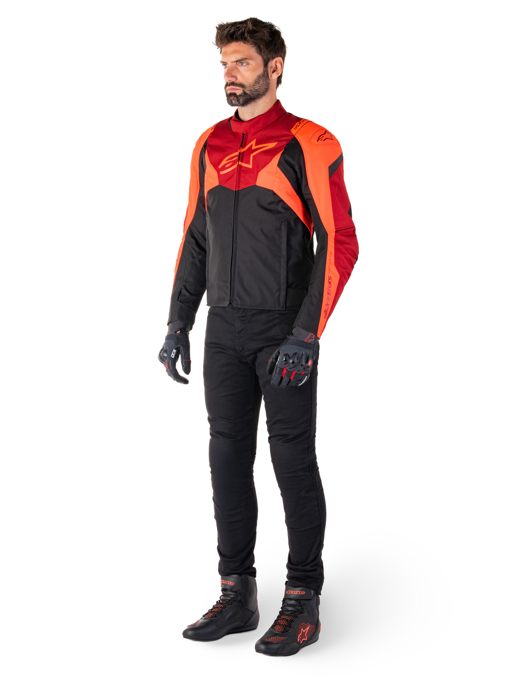 Motociclista che indossa la giacca Alpinestars T-Jaws V4 Waterproof in Nero Rosso Fluo Rosso Scuro, abbinata a pantaloni da moto neri, guanti e stivali da moto, con design sportivo in tessuto, logo sul petto e silhouette aggressiva