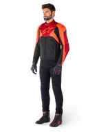 Motociclista che indossa la giacca Alpinestars T-Jaws V4 Waterproof in Nero Rosso Fluo Rosso Scuro, abbinata a pantaloni da moto neri, guanti e stivali da moto, con design sportivo in tessuto, logo sul petto e silhouette aggressiva