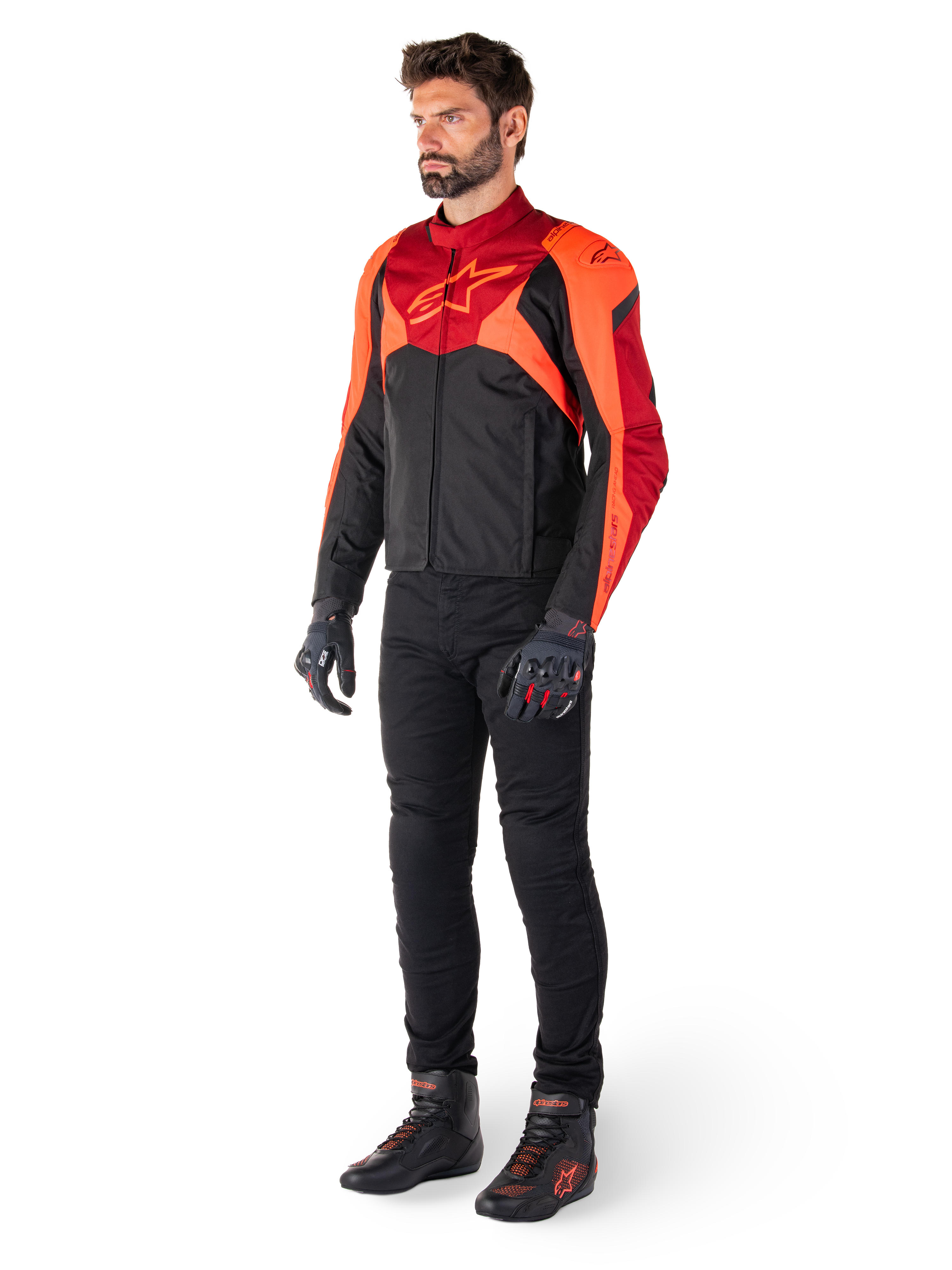 Motociclista che indossa la giacca Alpinestars T-Jaws V4 Waterproof in Nero Rosso Fluo Rosso Scuro, abbinata a pantaloni da moto neri, guanti e stivali da moto, con design sportivo in tessuto, logo sul petto e silhouette aggressiva