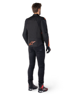 Giacca Alpinestars T-Jaws V4 Waterproof, nero e rosso fluo, vista posteriore indossata da un motociclista, con un vivace logo rosso fluo sulla schiena, abbinata a pantaloni da moto neri e stivali tecnici, abbigliamento sportivo da moto