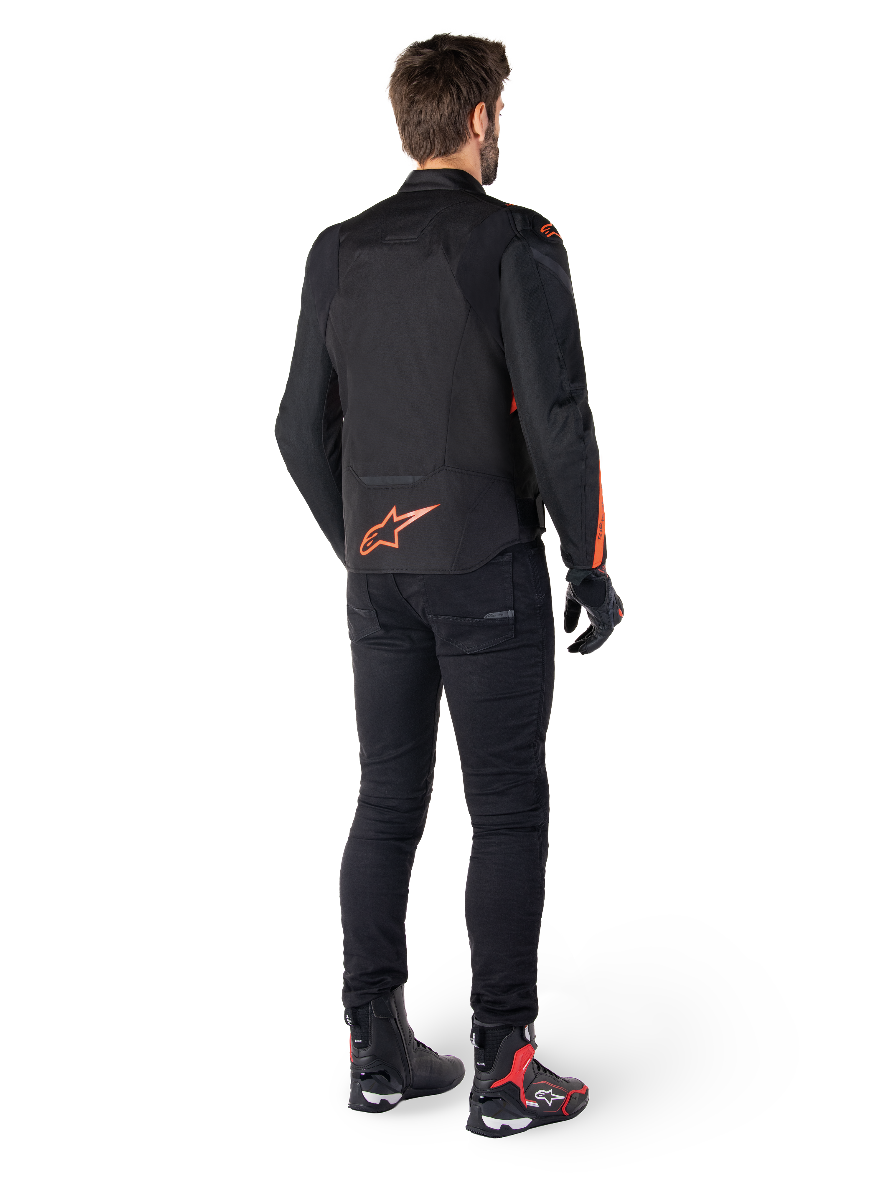 Giacca Alpinestars T-Jaws V4 Waterproof, nero e rosso fluo, vista posteriore indossata da un motociclista, con un vivace logo rosso fluo sulla schiena, abbinata a pantaloni da moto neri e stivali tecnici, abbigliamento sportivo da moto
