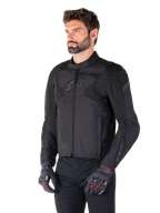 Motociclista che indossa la giacca impermeabile Alpinestars T-Jaws V4 in Black Black, abbinata a pantaloni neri e guanti protettivi, caratterizzata da una vestibilità sportiva, loghi Alpinestars tonali sul petto e sulle spalle e una struttura in tessuto ad alte prestazioni.
