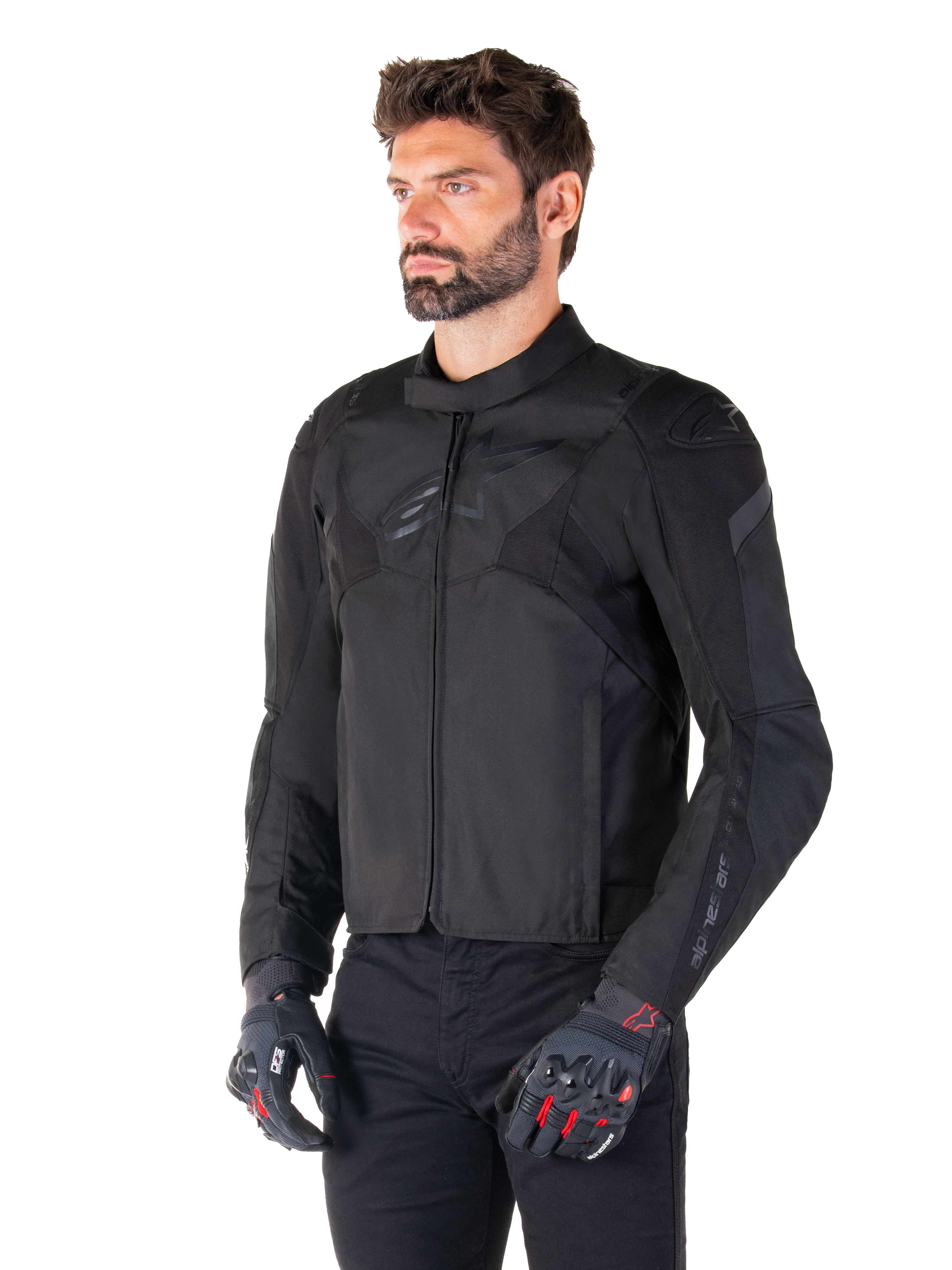 Motociclista che indossa la giacca impermeabile Alpinestars T-Jaws V4 in Black Black, abbinata a pantaloni neri e guanti protettivi, caratterizzata da una vestibilità sportiva, loghi Alpinestars tonali sul petto e sulle spalle e una struttura in tessuto ad alte prestazioni.
