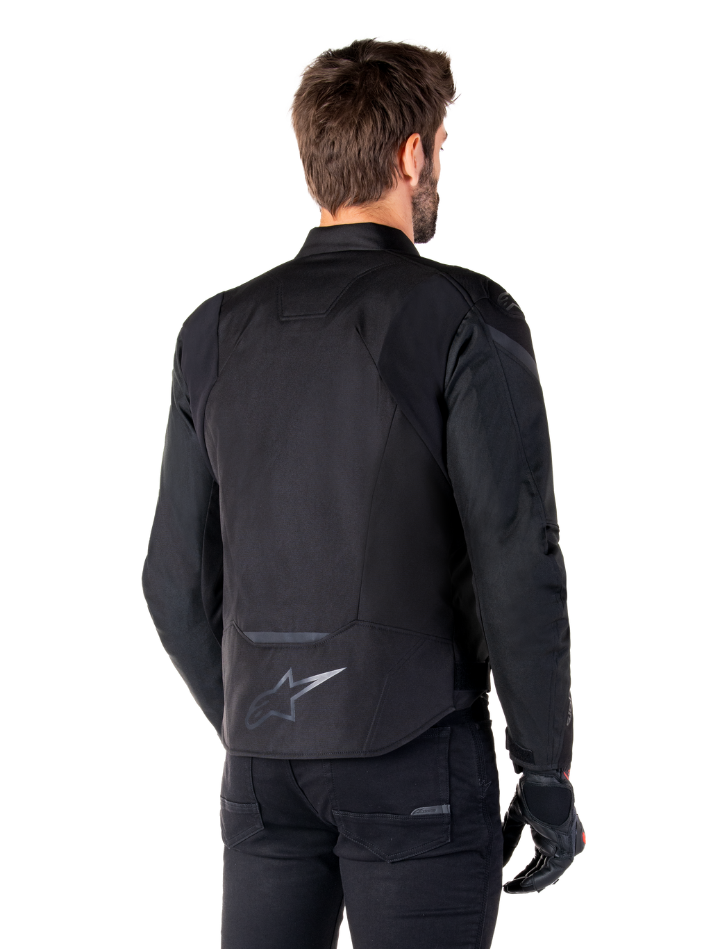 Giacca Alpinestars T-Jaws V4 Waterproof, nero, vista posteriore su modello, con logo Alpinestars riflettente sulla parte bassa della schiena, dorso allungato per una maggiore copertura, design sportivo in tessuto con pannelli tono su tono, indossata con guanti da moto neri