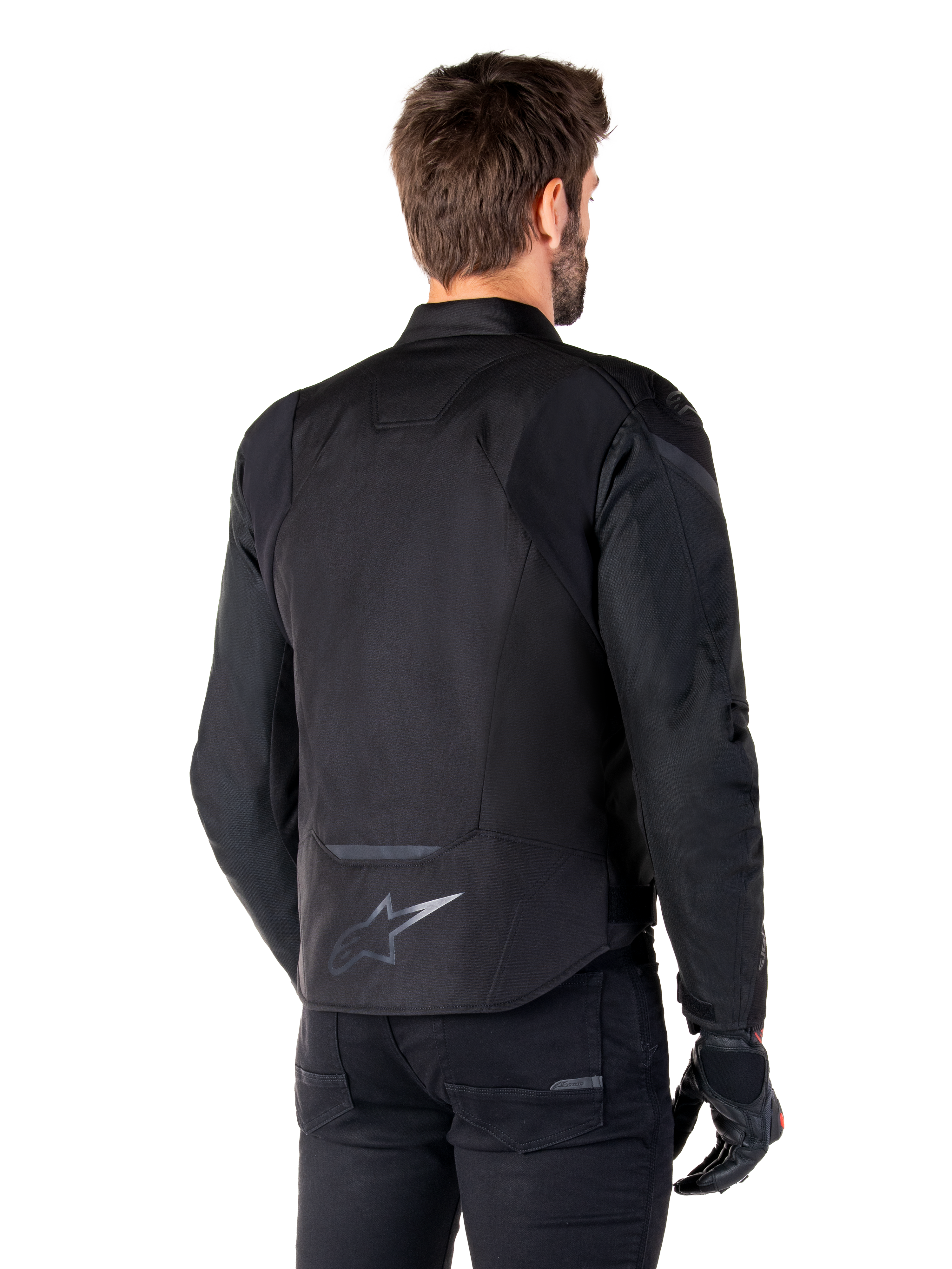 Giacca Alpinestars T-Jaws V4 Waterproof, nero, vista posteriore su modello, con logo Alpinestars riflettente sulla parte bassa della schiena, dorso allungato per una maggiore copertura, design sportivo in tessuto con pannelli tono su tono, indossata con guanti da moto neri