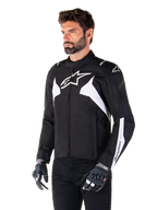 Giacca Alpinestars T-Jaws V4 Waterproof, nero e bianco, indossata da un modello con guanti da moto, con loghi Alpinestars e dettagli bianchi in evidenza, giacca da moto in tessuto con vestibilità sportiva per la guida su strada