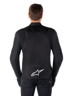 Giacca Alpinestars T-Jaws V4 Waterproof, giacca da moto nera vista dal retro, logo Alpinestars bianco sulla parte bassa della schiena, schiena allungata per maggiore copertura, indossata con pantaloni e guanti neri, design sportivo in tessuto