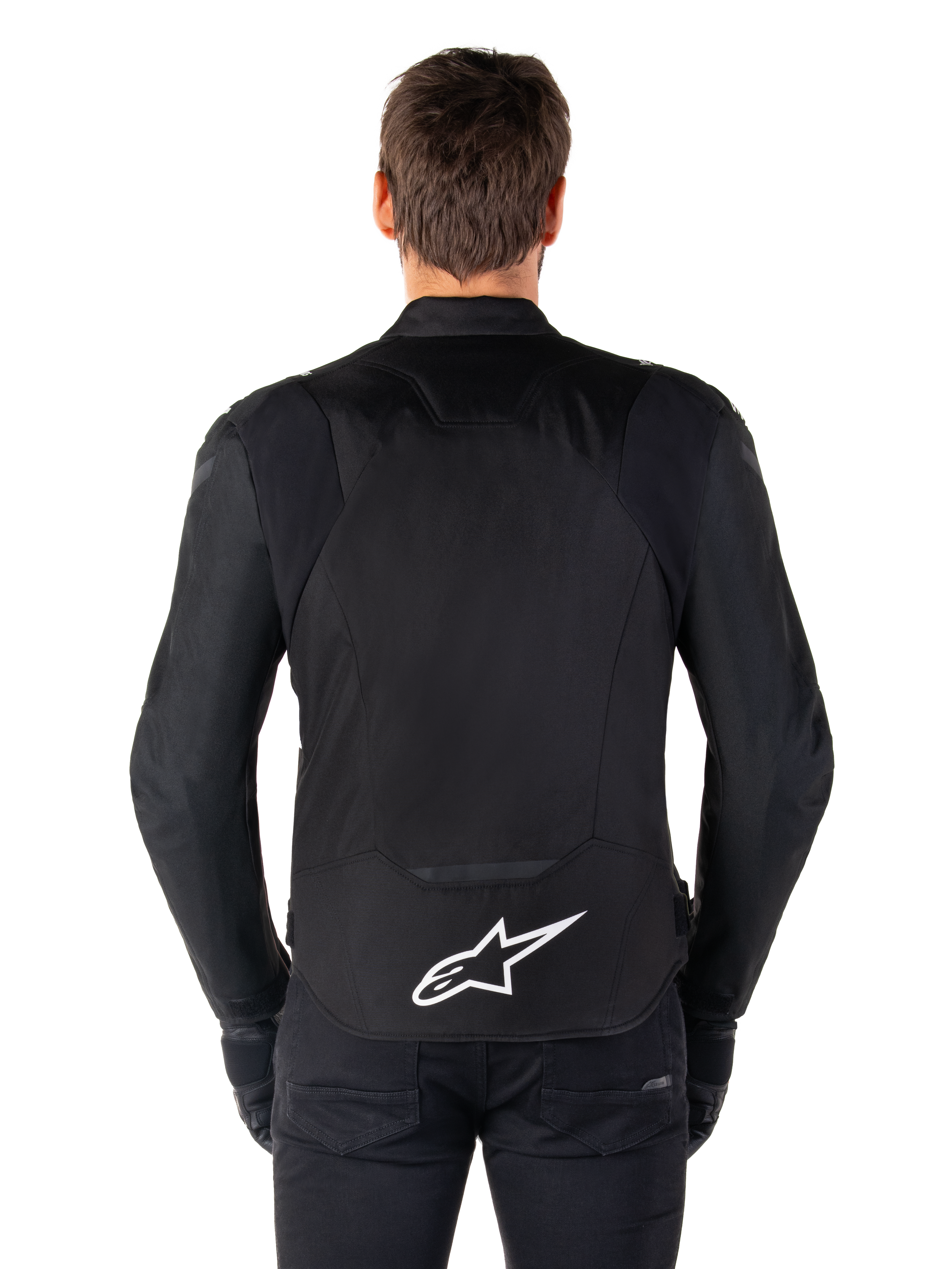 Giacca Alpinestars T-Jaws V4 Waterproof, giacca da moto nera vista dal retro, logo Alpinestars bianco sulla parte bassa della schiena, schiena allungata per maggiore copertura, indossata con pantaloni e guanti neri, design sportivo in tessuto