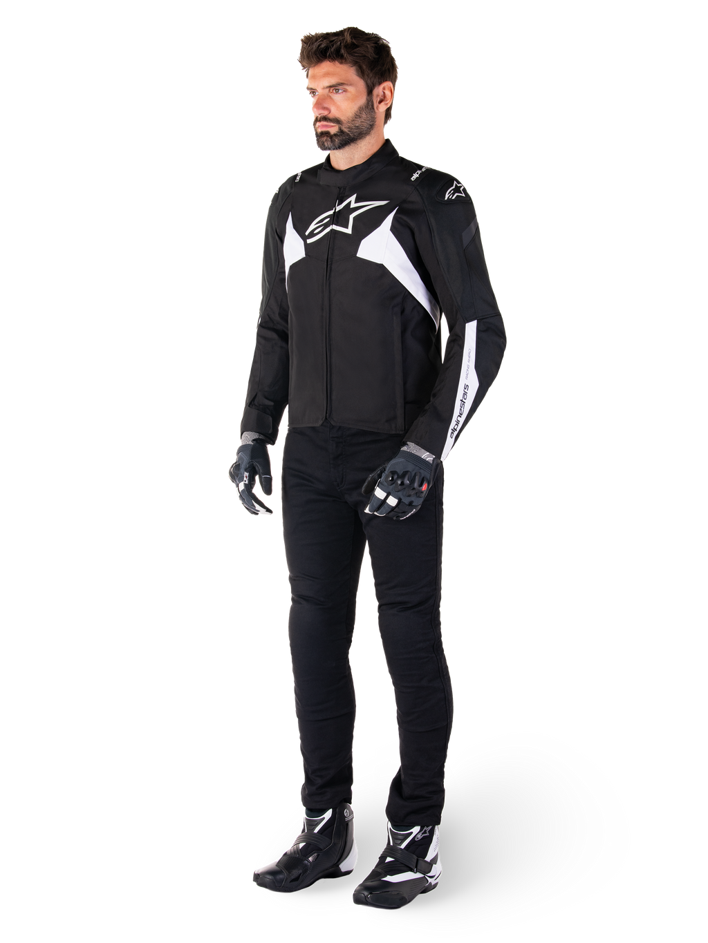 Modello che indossa la giacca impermeabile Alpinestars T-Jaws V4 in nero e bianco, giacca sportiva in tessuto con logo a stella bianco e dettagli sulle maniche, abbinata a pantaloni, guanti e stivali da moto neri per un look completo da guida su strada