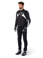 Modello che indossa la giacca impermeabile Alpinestars T-Jaws V4 in nero e bianco, giacca sportiva in tessuto con logo a stella bianco e dettagli sulle maniche, abbinata a pantaloni, guanti e stivali da moto neri per un look completo da guida su strada
