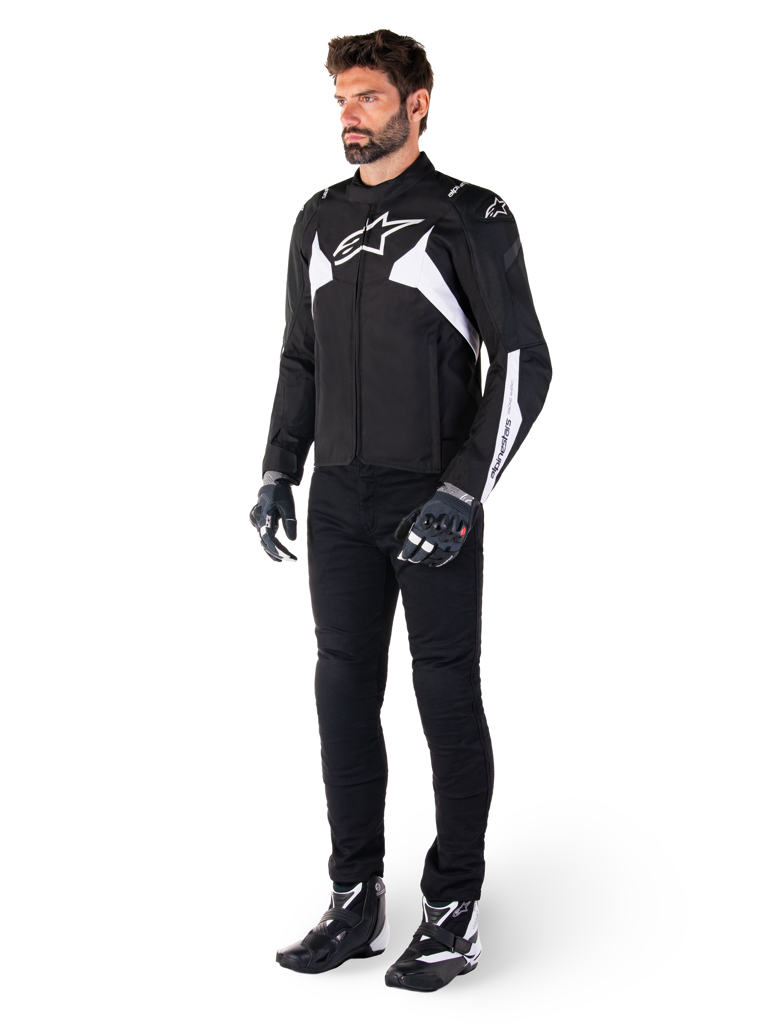 Modello che indossa la giacca impermeabile Alpinestars T-Jaws V4 in nero e bianco, giacca sportiva in tessuto con logo a stella bianco e dettagli sulle maniche, abbinata a pantaloni, guanti e stivali da moto neri per un look completo da guida su strada