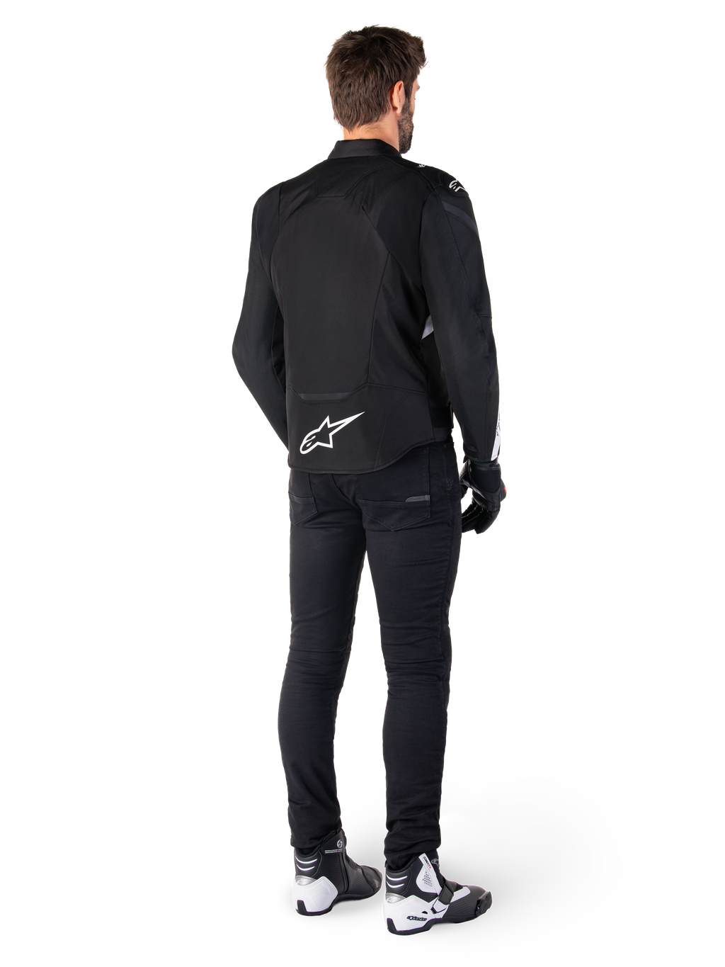Giacca impermeabile Alpinestars T-Jaws V4, bianco e nero, vista posteriore con logo a stella bianca sulla parte bassa della schiena, indossata da un modello con pantaloni da guida neri, guanti neri e stivali da moto bianchi e neri