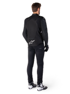 Giacca impermeabile Alpinestars T-Jaws V4, bianco e nero, vista posteriore con logo a stella bianca sulla parte bassa della schiena, indossata da un modello con pantaloni da guida neri, guanti neri e stivali da moto bianchi e neri