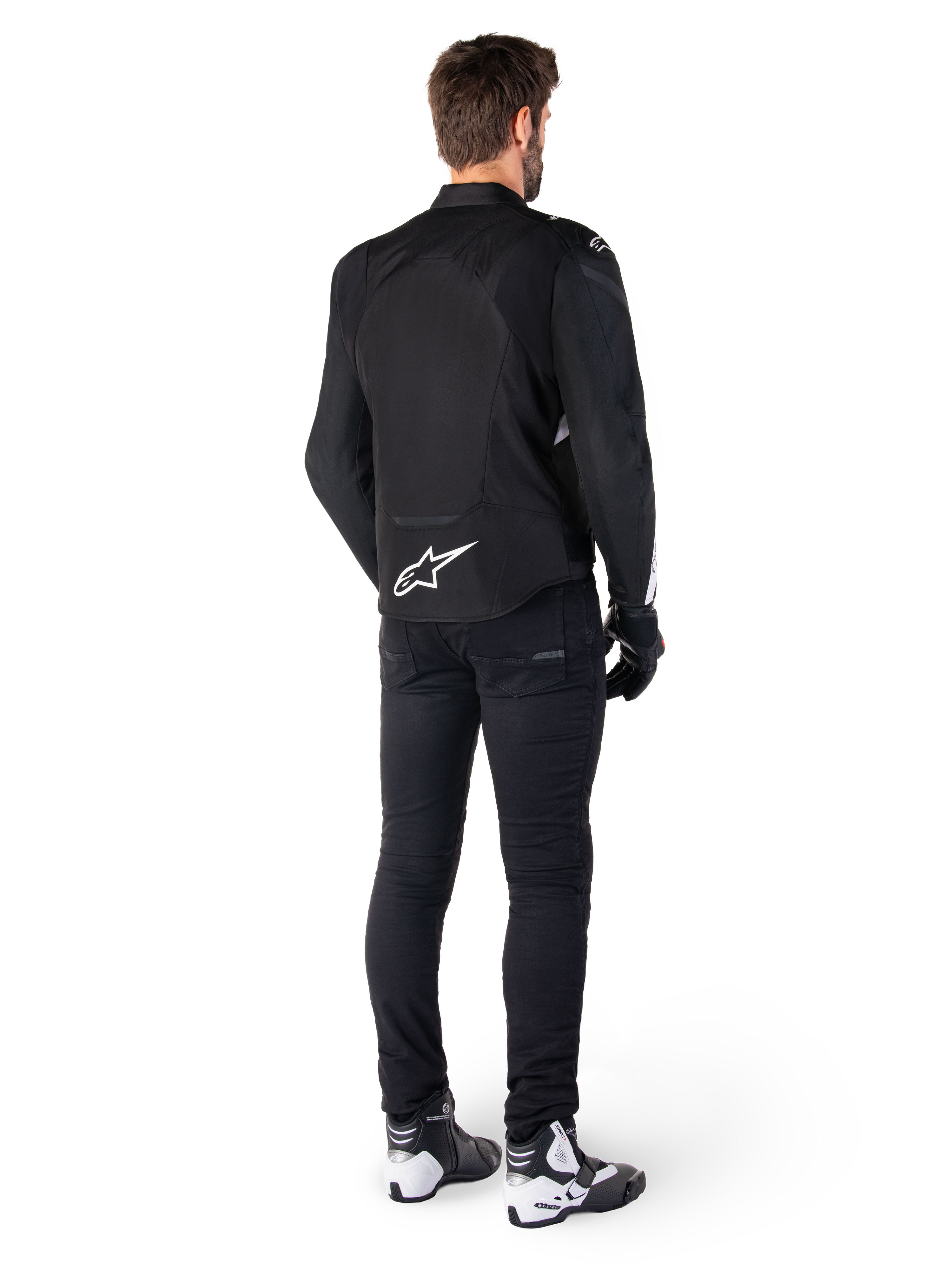Giacca impermeabile Alpinestars T-Jaws V4, bianco e nero, vista posteriore con logo a stella bianca sulla parte bassa della schiena, indossata da un modello con pantaloni da guida neri, guanti neri e stivali da moto bianchi e neri
