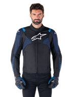 Giacca Alpinestars T-Jaws V4 Waterproof, giacca da moto, nero e blu scuro con accenti blu Blithe, logo bianco sul petto, scritte blu sulle spalle, indossata con guanti abbinati, abbigliamento tecnico da moto in tessuto impermeabile