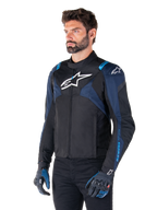 Alpinestars T-Jaws V4 Waterproof Jacket, giacca da moto, nero, blu scuro e blu Blithe, indossata da un modello con guanti coordinati e pantaloni neri, con loghi Alpinestars bianchi su petto e spalle e dettagli blu sulle maniche, abbigliamento tecnico sportivo in tessuto