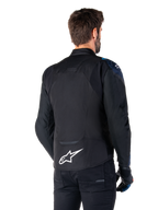 Alpinestars T-Jaws V4 Waterproof Jacket, vista posteriore, nero con dettagli Dark Blue e Blithe Blue, logo a stella bianco sulla parte bassa della schiena, silhouette sportiva, indossata con pantaloni neri e guanti da moto