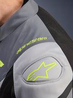 Giacca impermeabile Alpinestars T-Jaws V4, dettaglio della spalla con logo e scritta Alpinestars in giallo neon, tessuto tecnico Black Ice Gray e Dark Gray, rinforzo della spalla GP Lite.