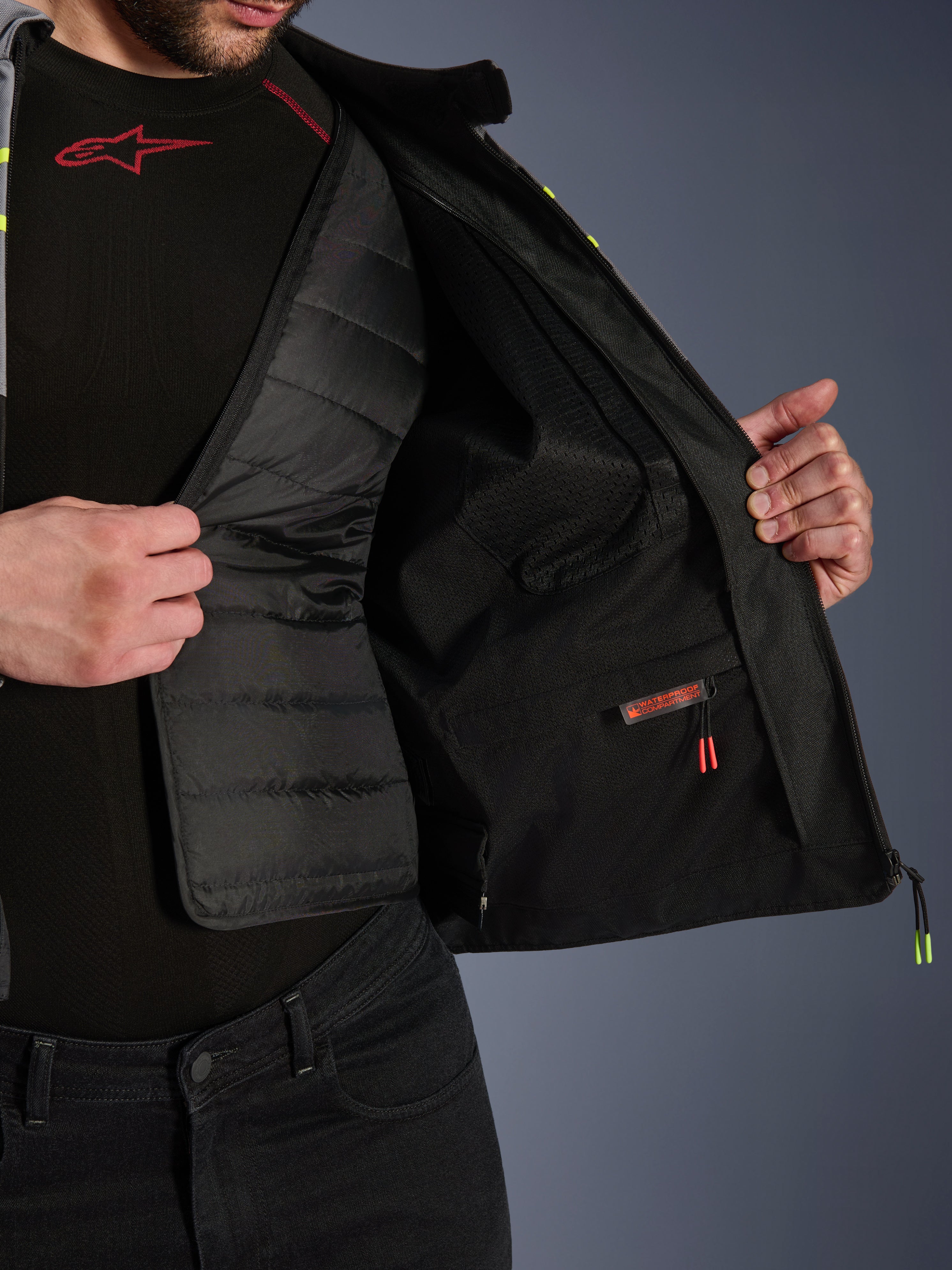 Vista interna della giacca Alpinestars T-Jaws V4 Waterproof, mostra la fodera termica trapuntata nera rimovibile e lo scomparto interno impermeabile con etichetta rossa, fodera in rete, abbigliamento protettivo da moto di alta qualità