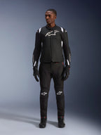 Giacca Impermeabile Alpinestars T-SP 1 V2, nero e bianco, con un prominente logo bianco sul petto e accenti sulle spalle, indossata con pantaloni e guanti da moto neri coordinati per un look da strada completo