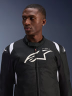 Giacca impermeabile Alpinestars T-SP 1 V2 indossata da un modello, giacca da moto in tessuto bianco e nero, grande logo Alpinestars bianco e marchio T-SP-1 sul petto, design sportivo con slider protettivi sulle spalle