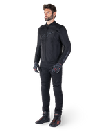 Giacca impermeabile Alpinestars T-SPS V2, nero, indossata da un modello con pantaloni neri coordinati, guanti neri con dettagli rossi e scarpe da moto nere, equipaggiamento completo da moto per guida urbana e sportiva, sfondo bianco