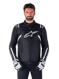 Giacca Alpinestars T-SPS V2 Waterproof in nero e bianco, vista frontale su modello, giacca da moto impermeabile in tessuto con strisce bianche su spalle e braccia, grande logo Alpinestars bianco sul petto, indossata con guanti protettivi da moto, silhouette sportiva ed elegante