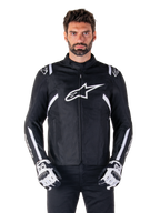 Giacca Alpinestars T-SPS V2 Waterproof in nero e bianco, vista frontale su modello, giacca da moto impermeabile in tessuto con strisce bianche su spalle e braccia, grande logo Alpinestars bianco sul petto, indossata con guanti protettivi da moto, silhouette sportiva ed elegante