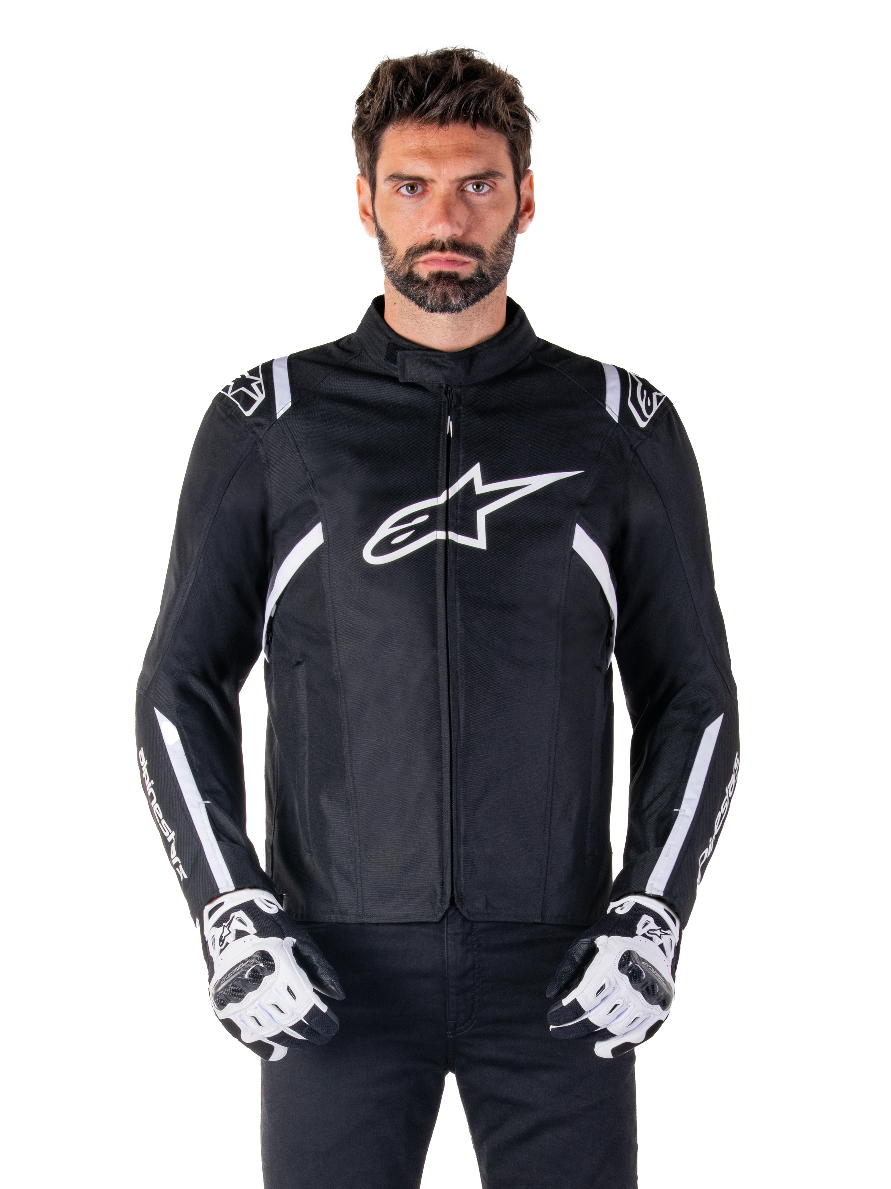 Giacca Alpinestars T-SPS V2 Waterproof in nero e bianco, vista frontale su modello, giacca da moto impermeabile in tessuto con strisce bianche su spalle e braccia, grande logo Alpinestars bianco sul petto, indossata con guanti protettivi da moto, silhouette sportiva ed elegante
