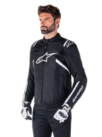 Giacca Alpinestars T-SPS V2 Waterproof, nero e bianco, indossata da un modello con guanti da moto coordinati, giacca in tessuto dal taglio sportivo con loghi Alpinestars bianchi su petto e spalle, marchio 'alpinestars T-SPS' sulla manica, abbigliamento da moto elegante d'ispirazione racing