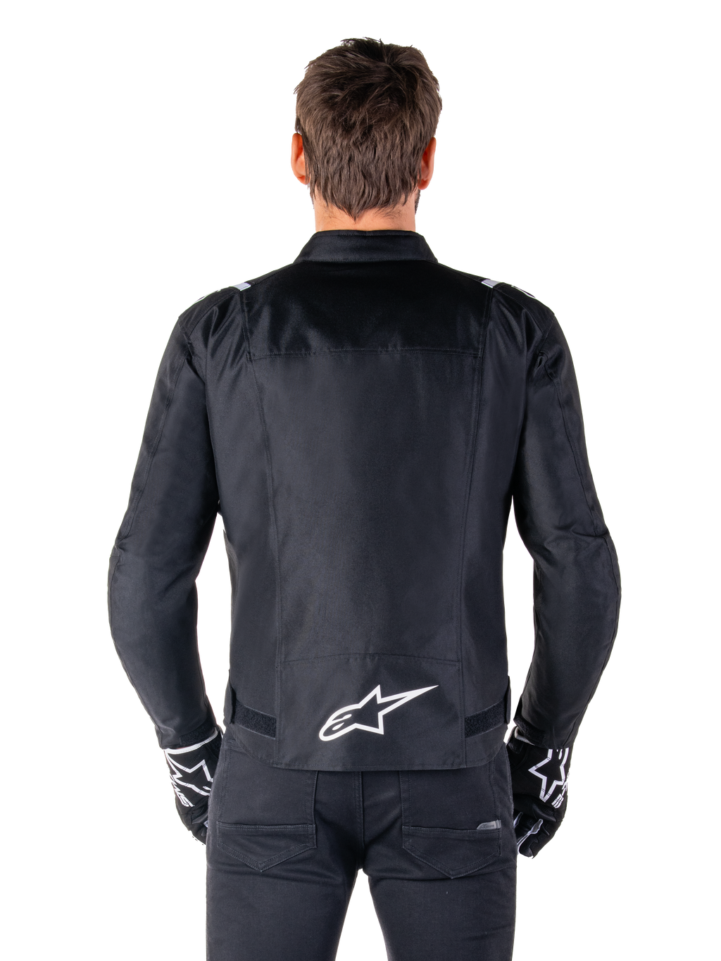 Giacca Alpinestars T-SPS V2 Waterproof, nero e bianco, vista posteriore con logo Alpinestars bianco sulla parte bassa della schiena, indossata con pantaloni e guanti neri, giacca da moto in tessuto con taglio sportivo