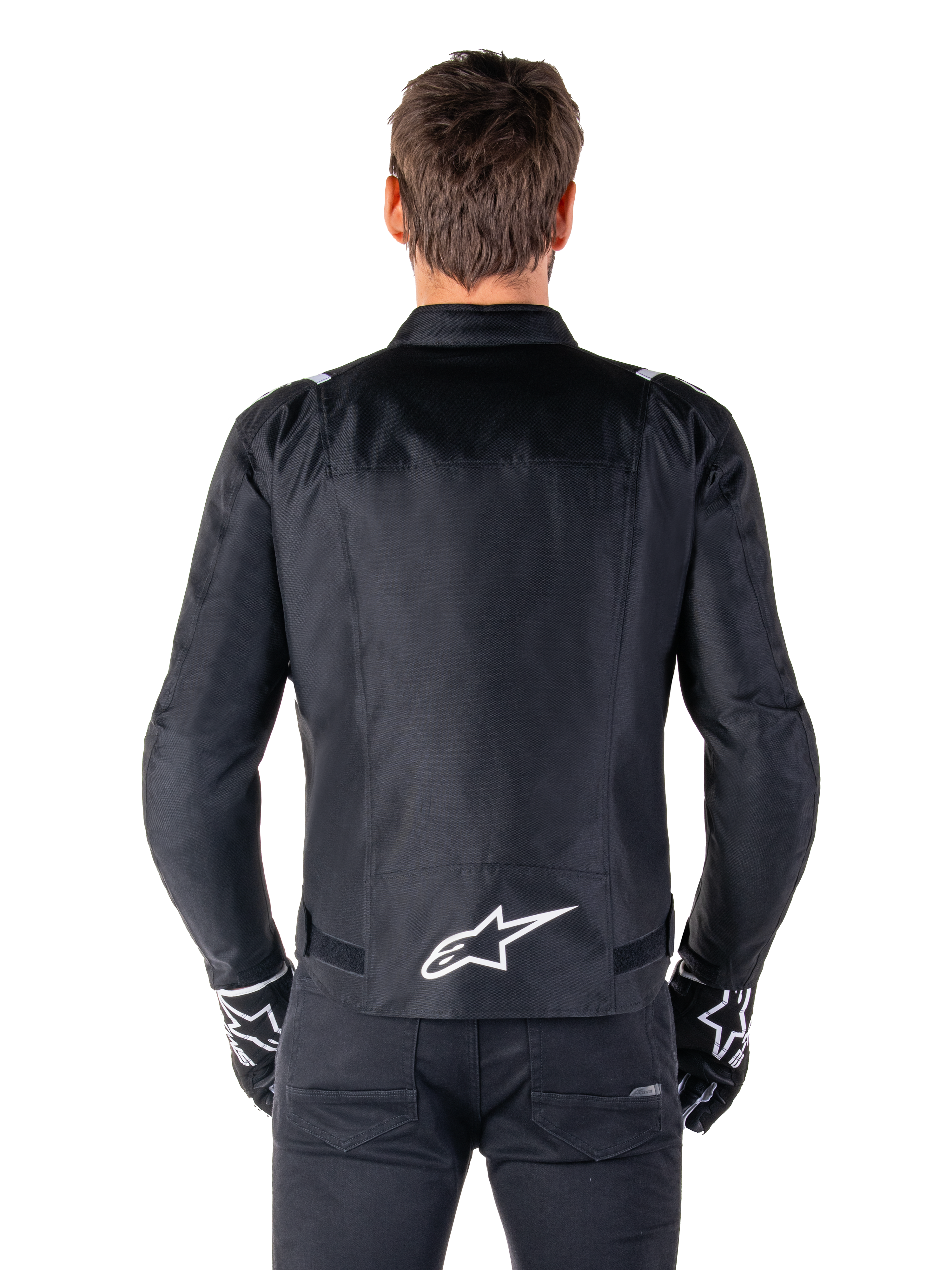 Giacca Alpinestars T-SPS V2 Waterproof, nero e bianco, vista posteriore con logo Alpinestars bianco sulla parte bassa della schiena, indossata con pantaloni e guanti neri, giacca da moto in tessuto con taglio sportivo