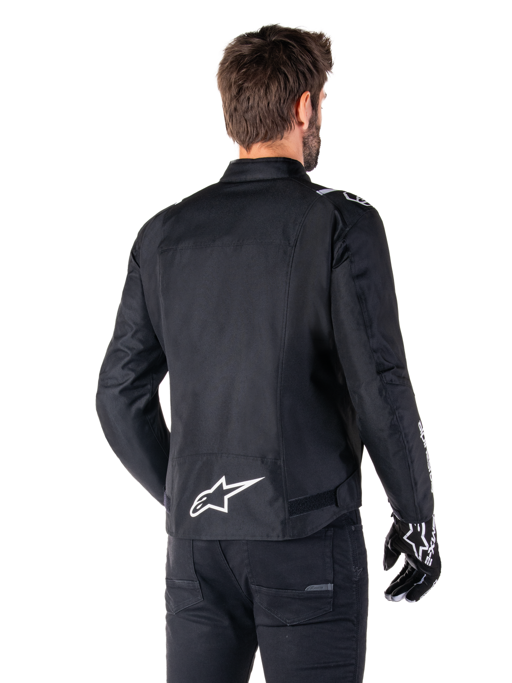 Giacca Alpinestars T-SPS V2 Waterproof, nero e bianco, vista posteriore di un motociclista che indossa la giacca, logo Alpinestars bianco sulla parte bassa della schiena, struttura in tessuto con taglio sportivo, indossata con pantaloni da moto e guanti neri