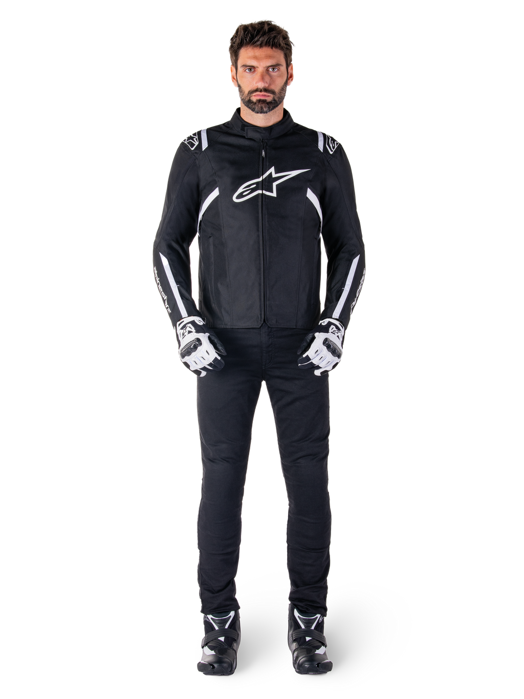 Giacca impermeabile Alpinestars T-SPS V2, nero e bianco, indossata da un modello uomo con pantaloni neri e guanti coordinati, con logo Alpinestars bianco sul petto e dettagli sulle maniche, silhouette dal taglio sportivo per la guida in moto in ogni condizione atmosferica