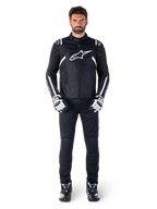 Giacca impermeabile Alpinestars T-SPS V2, nero e bianco, indossata da un modello uomo con pantaloni neri e guanti coordinati, con logo Alpinestars bianco sul petto e dettagli sulle maniche, silhouette dal taglio sportivo per la guida in moto in ogni condizione atmosferica
