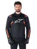 Giacca impermeabile Alpinestars T-SPS V2, nero, bianco e rosso fluo, indossata da un modello con guanti da moto neri, caratterizzata da un grande logo Alpinestars bianco sul petto e vivaci dettagli arancioni sulle spalle e sulle maniche.