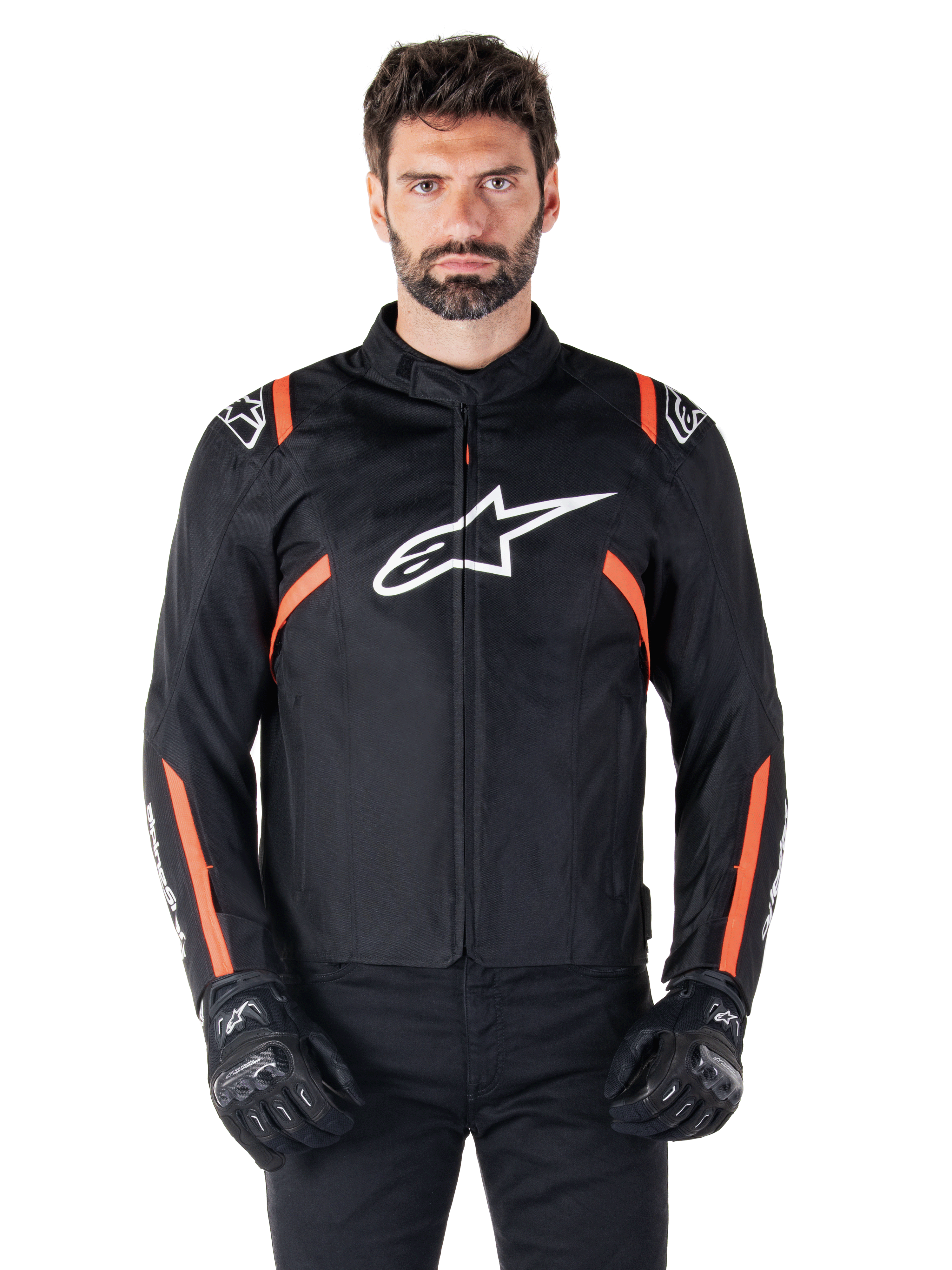 Giacca impermeabile Alpinestars T-SPS V2, nero, bianco e rosso fluo, indossata da un modello con guanti da moto neri, caratterizzata da un grande logo Alpinestars bianco sul petto e vivaci dettagli arancioni sulle spalle e sulle maniche.