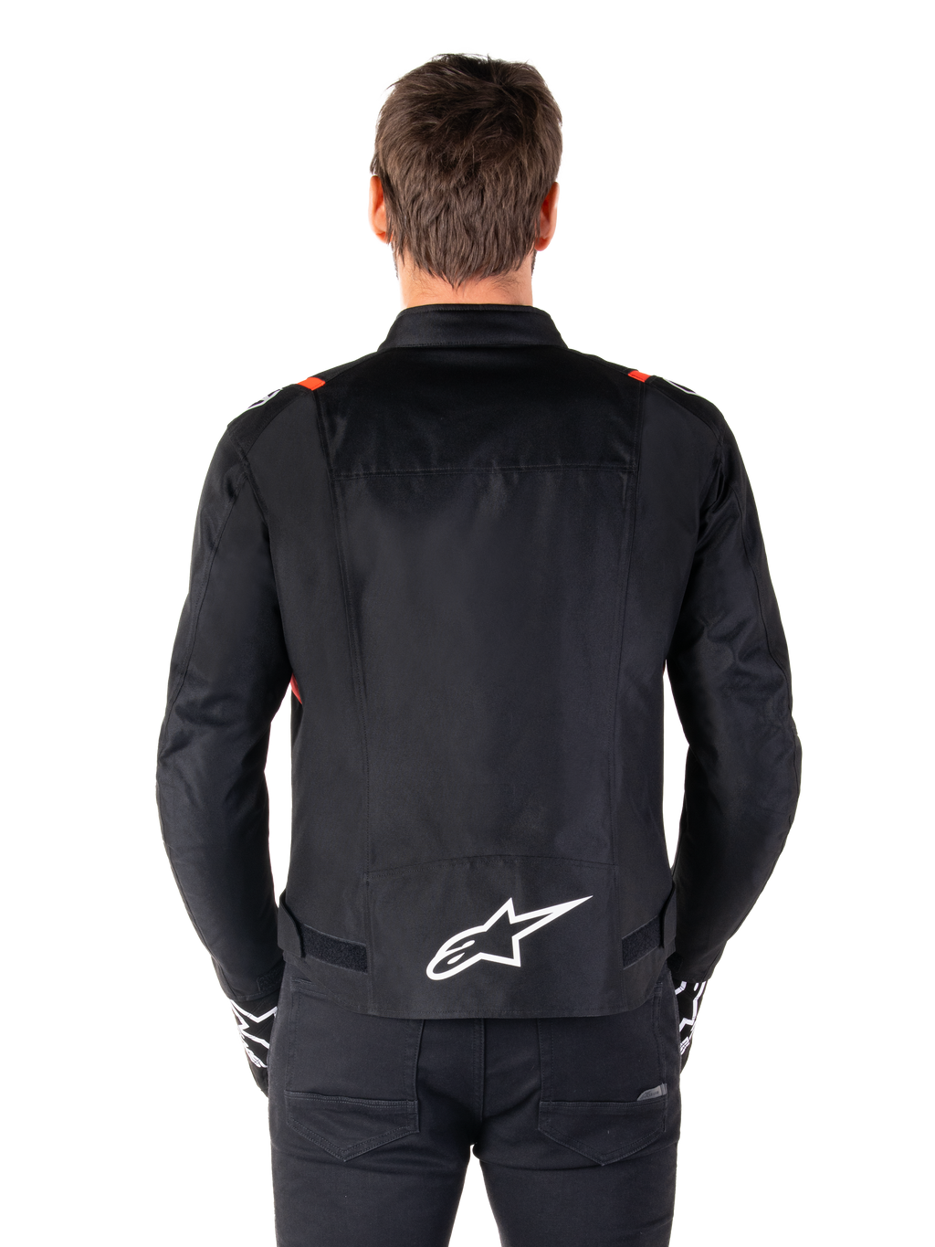 Giacca Alpinestars T-SPS V2 Waterproof, nero con accenti bianco e rosso fluo, vista posteriore con grande logo Alpinestars bianco sulla parte bassa della schiena, giacca da moto in tessuto dal taglio sportivo, indossata con pantaloni e guanti neri