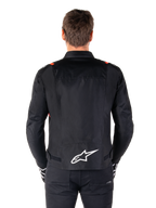 Giacca Alpinestars T-SPS V2 Waterproof, nero con accenti bianco e rosso fluo, vista posteriore con grande logo Alpinestars bianco sulla parte bassa della schiena, giacca da moto in tessuto dal taglio sportivo, indossata con pantaloni e guanti neri