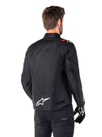 Giacca impermeabile Alpinestars T-SPS V2, nero bianco rosso fluo, vista posteriore, con logo Alpinestars bianco sulla parte bassa della schiena e dettagli rossi sulle spalle, indossata con guanti e pantaloni da moto neri, giacca da moto sportiva in tessuto.