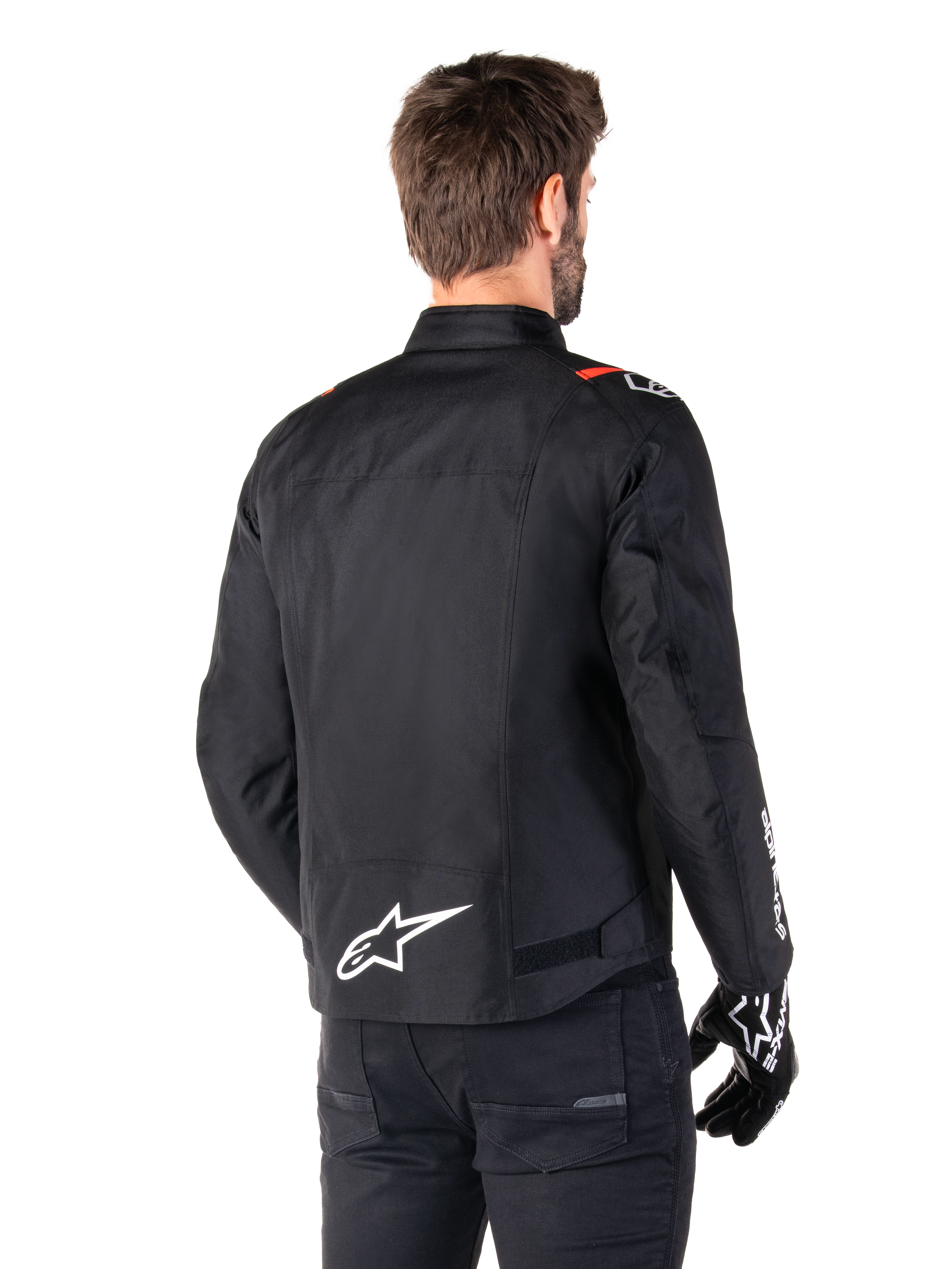 Giacca impermeabile Alpinestars T-SPS V2, nero bianco rosso fluo, vista posteriore, con logo Alpinestars bianco sulla parte bassa della schiena e dettagli rossi sulle spalle, indossata con guanti e pantaloni da moto neri, giacca da moto sportiva in tessuto.
