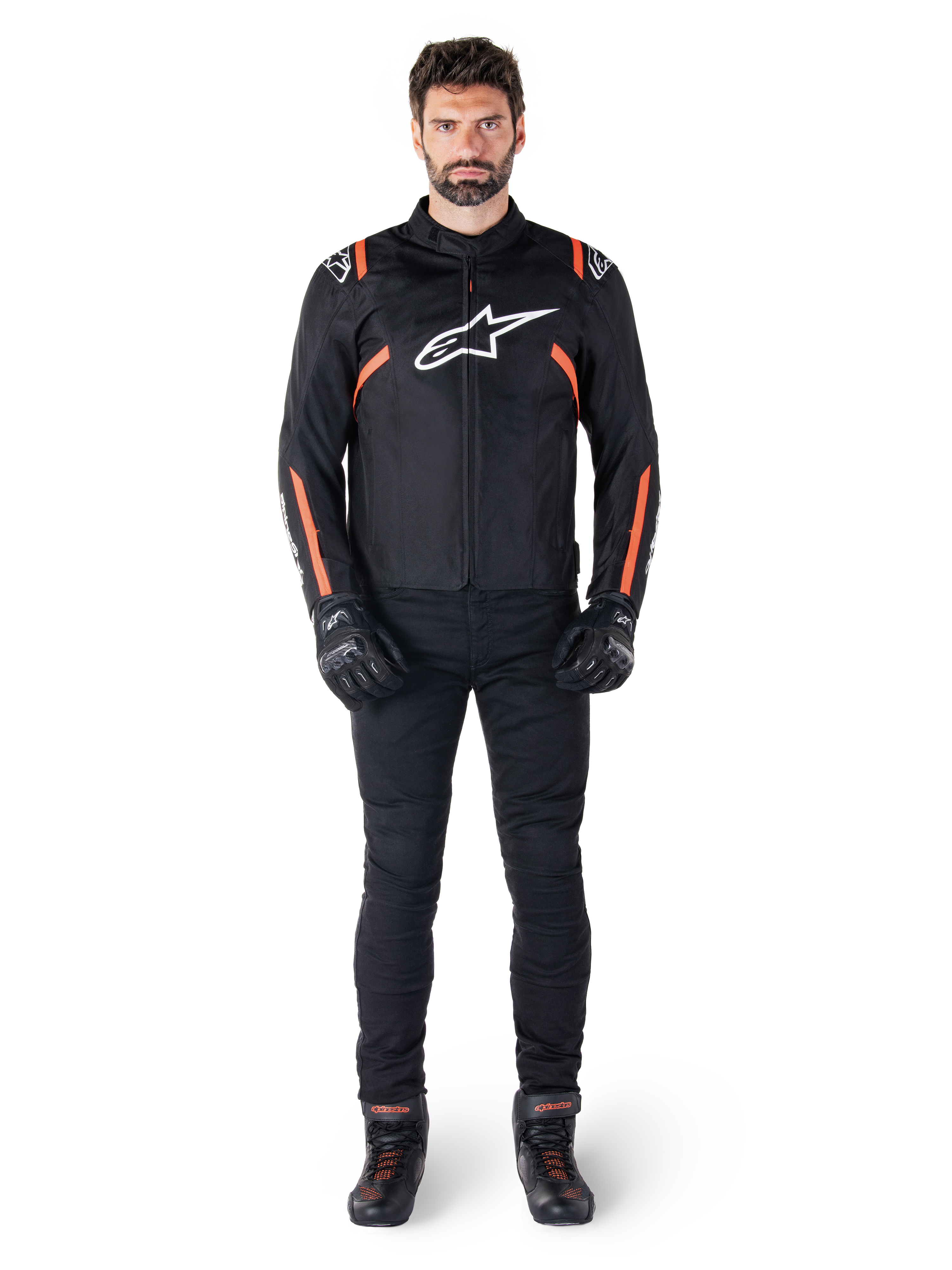 Modello che indossa la giacca Alpinestars T-SPS V2 Waterproof in Nero Bianco Rosso Fluo, abbinata a pantaloni da moto e guanti neri, con logo Alpinestars bianco sul petto e dettagli rossi sulle maniche.