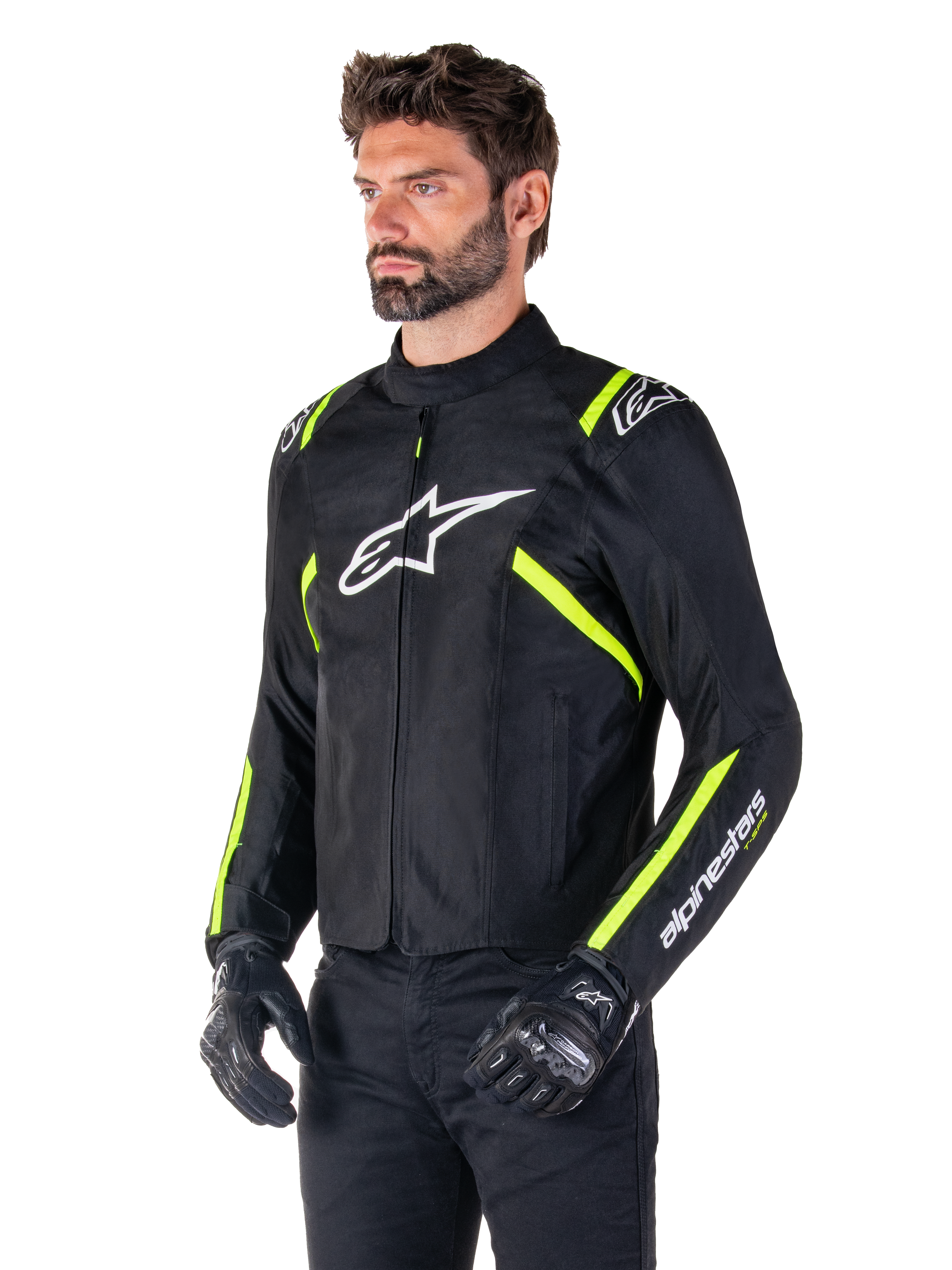 Modello che indossa la giacca impermeabile Alpinestars T-SPS V2, nero con dettagli bianco e giallo fluo, con logo Astars bianco sul petto e strisce giallo fluorescente su spalle e maniche, abbinata a pantaloni neri e guanti da guida, giacca da moto in tessuto dal taglio sportivo.