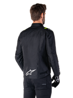 Alpinestars T-SPS V2 Waterproof Jacket, nero bianco giallo fluo, vista posteriore di un modello maschile che indossa la giacca da moto in tessuto, con logo bianco sulla parte bassa della schiena e accenti giallo fluo sulle spalle, abbinata a pantaloni e guanti neri.