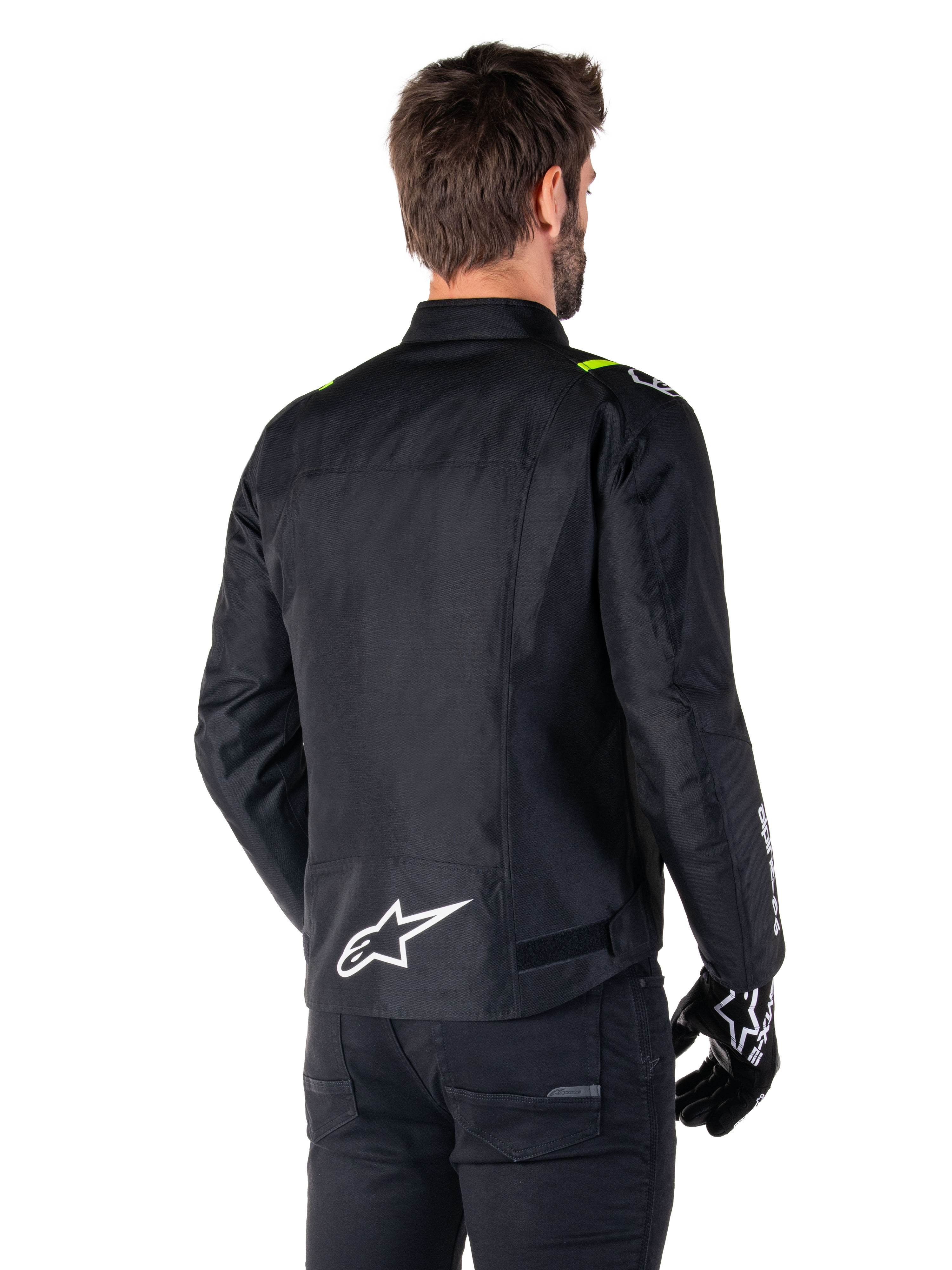 Alpinestars T-SPS V2 Waterproof Jacket, nero bianco giallo fluo, vista posteriore di un modello maschile che indossa la giacca da moto in tessuto, con logo bianco sulla parte bassa della schiena e accenti giallo fluo sulle spalle, abbinata a pantaloni e guanti neri.