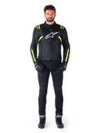 Giacca impermeabile Alpinestars T-SPS V2, nero, bianco e giallo fluo, indossata da un modello con pantaloni e guanti da moto neri, con logo Alpinestars bianco sul petto e dettagli fluorescenti su spalle e maniche, abbigliamento da moto dal taglio sportivo