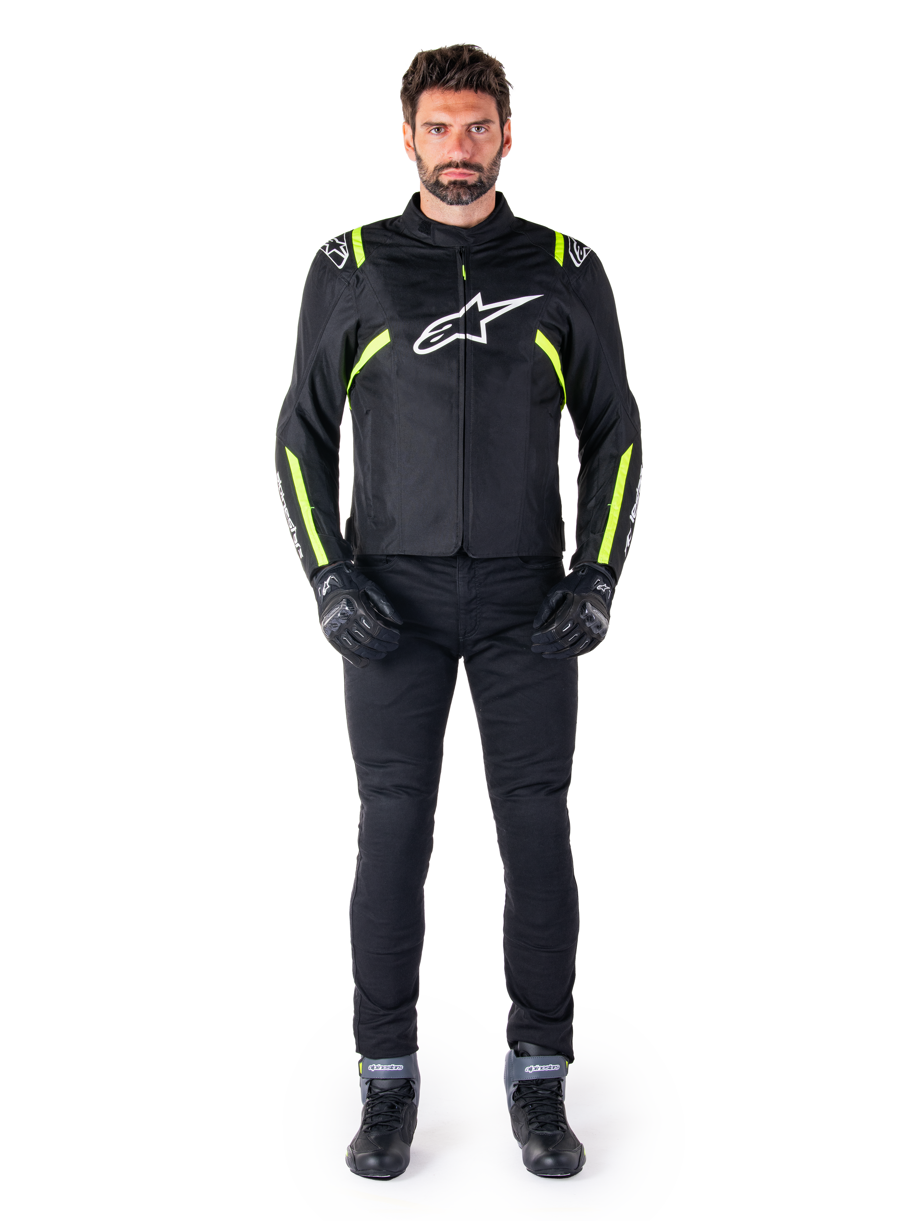 Giacca impermeabile Alpinestars T-SPS V2, nero, bianco e giallo fluo, indossata da un modello con pantaloni e guanti da moto neri, con logo Alpinestars bianco sul petto e dettagli fluorescenti su spalle e maniche, abbigliamento da moto dal taglio sportivo