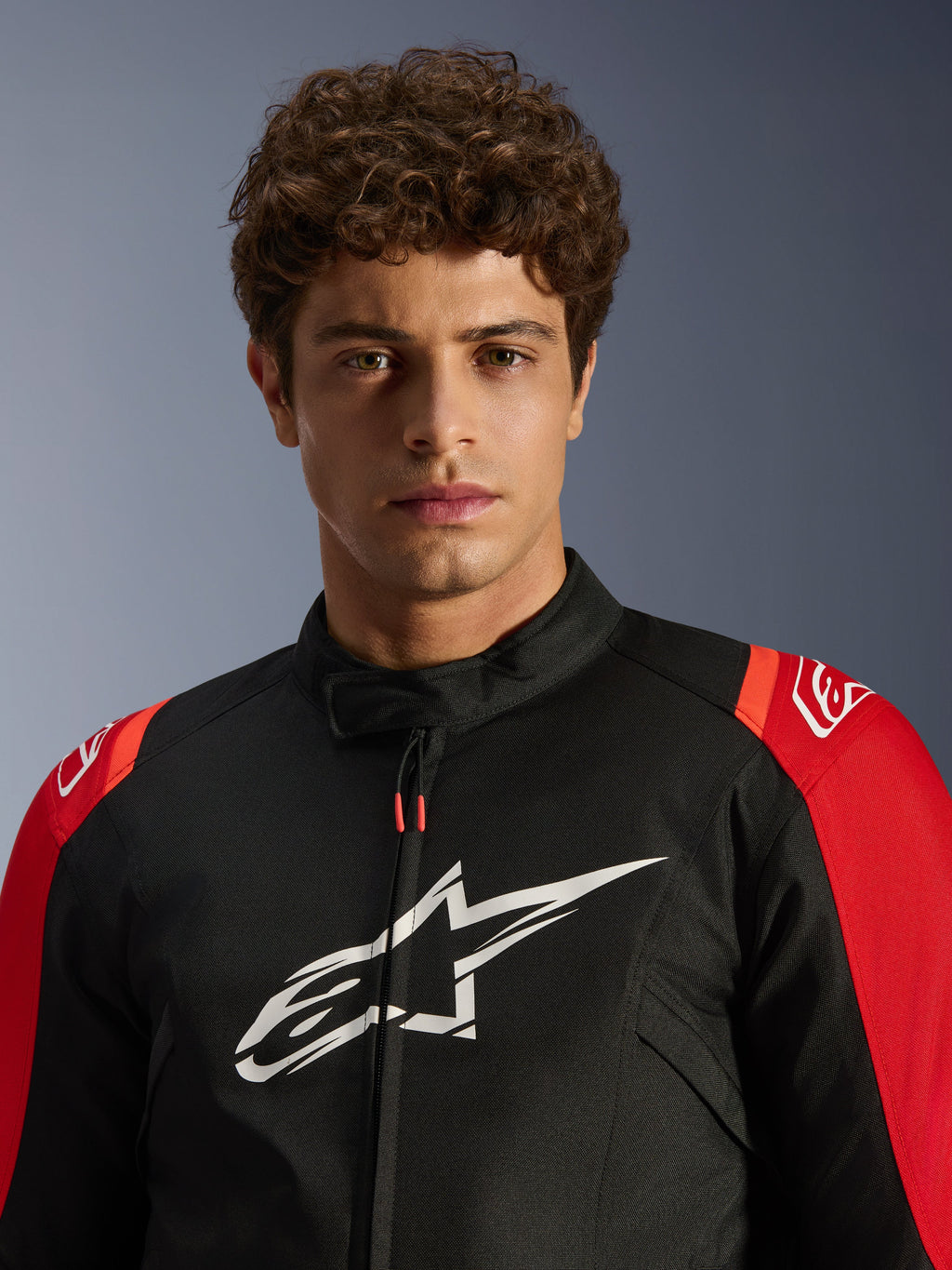 Modello maschile che indossa la giacca Alpinestars T-SPS V2 Waterproof, nera con dettagli rossi e logo bianco, primo piano, giacca da moto sportiva in tessuto