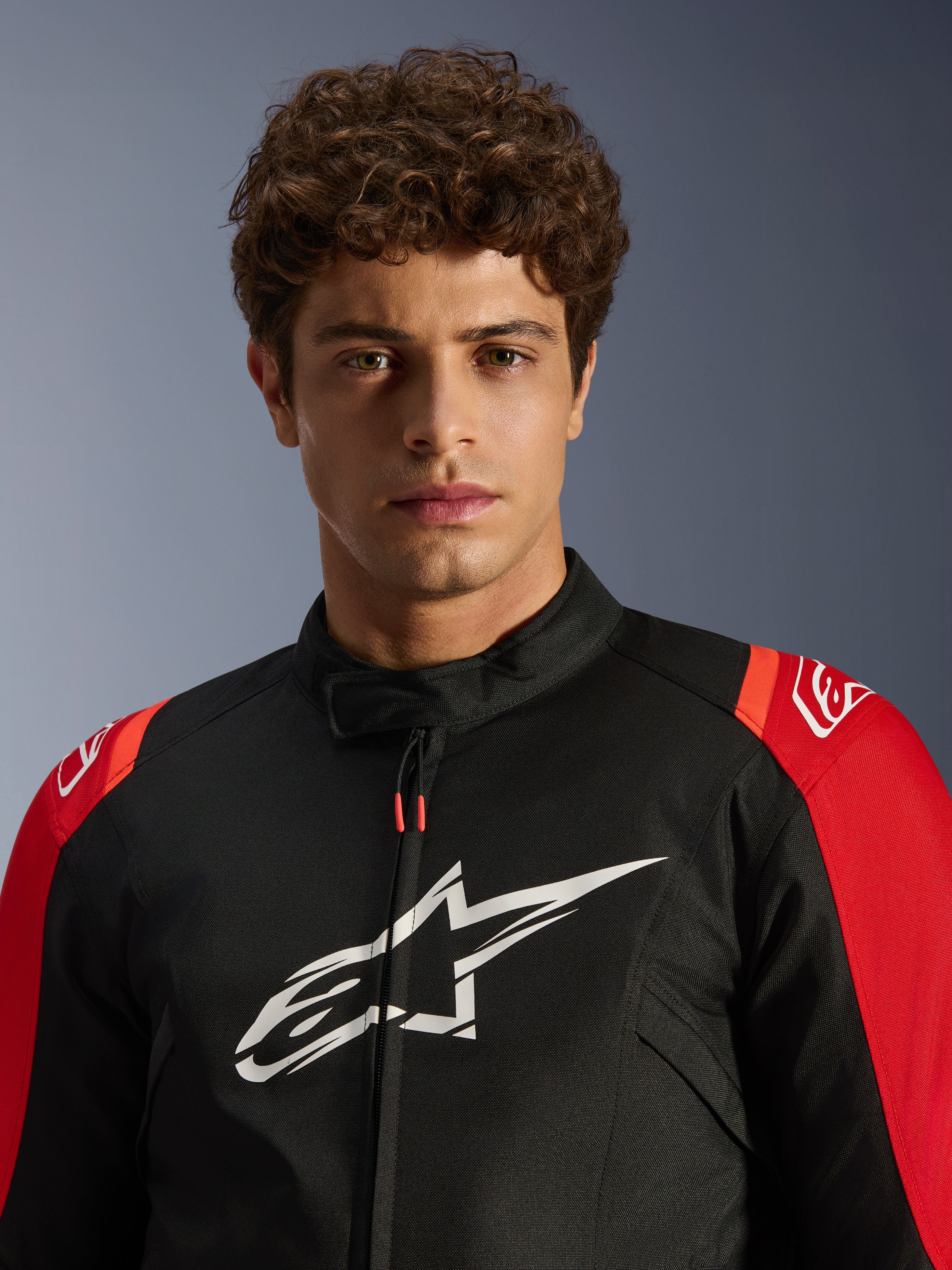 Modello maschile che indossa la giacca Alpinestars T-SPS V2 Waterproof, nera con dettagli rossi e logo bianco, primo piano, giacca da moto sportiva in tessuto