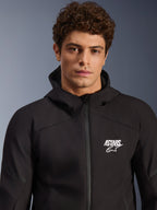 Modello che indossa la giacca Alpinestars Aeroshell Waterproof, felpa softshell in tessuto nero con cappuccio, logo ASTARS bianco sul petto, cerniera frontale impermeabile, ritratto moderno in studio per abbigliamento moto stradale